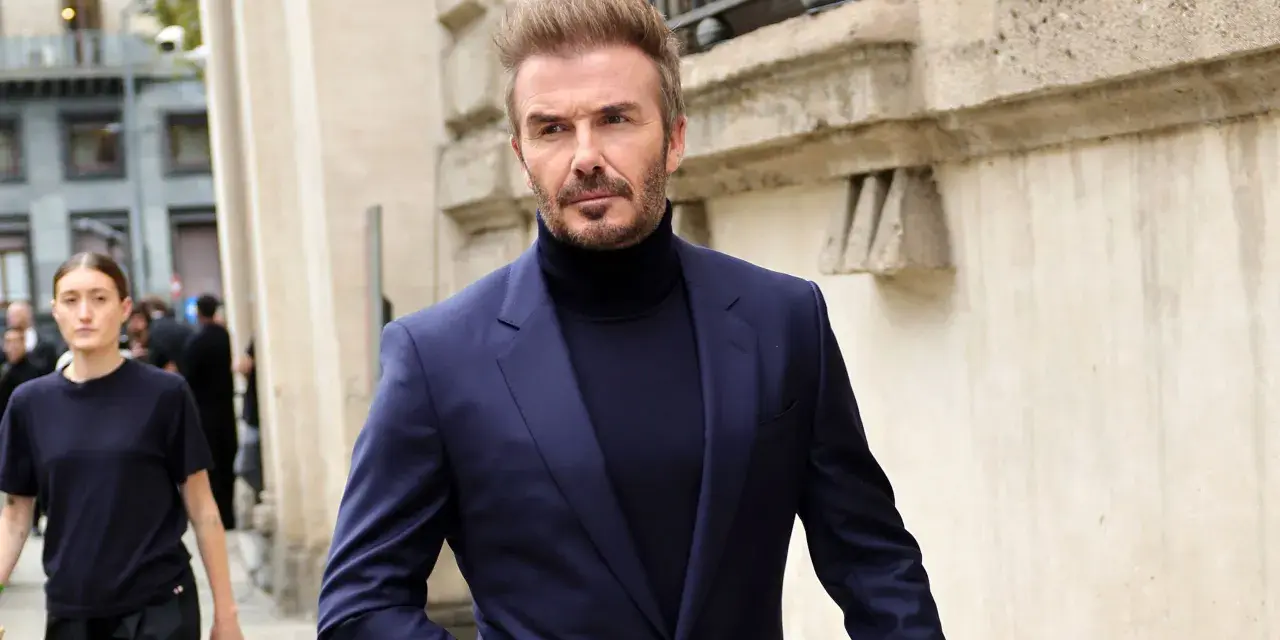 David Beckham luce un elegante traje azul con jersey de cuello alto, caminando con confianza.