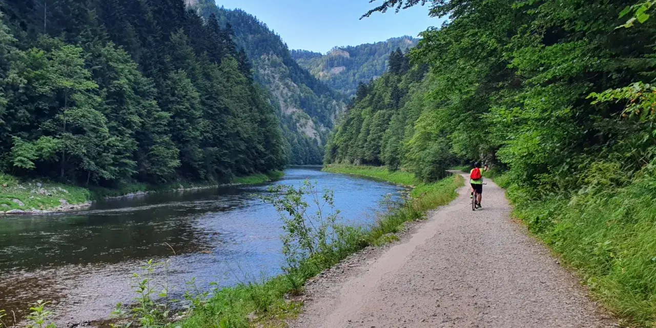 Rowerzysta przemierza malowniczą trasę velo dunajec w otoczeniu zielonych gór i spokojnej rzeki.