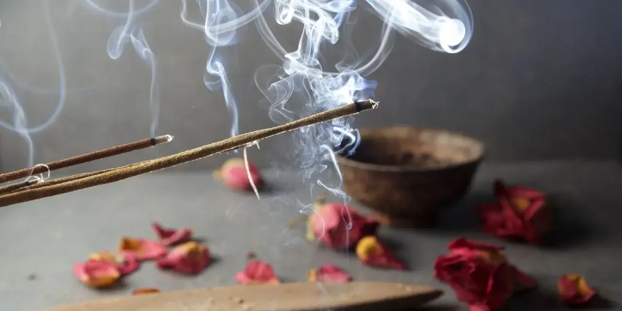 Humo de incienso de lavanda asciende, evocando paz y el significado espiritual de la calma. Pétalos secos y un cuenco completan la escena.