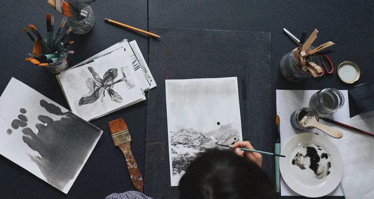 Osoba tworzy krajobraz podczas warsztatów malarskich dla początkujących. Widać pędzle, tusz i szkice.