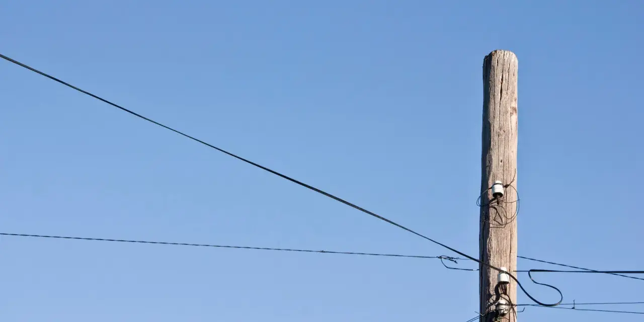 Słup energetyczny z przewodami, symbolizujący zgodę na światłowód nad działką.