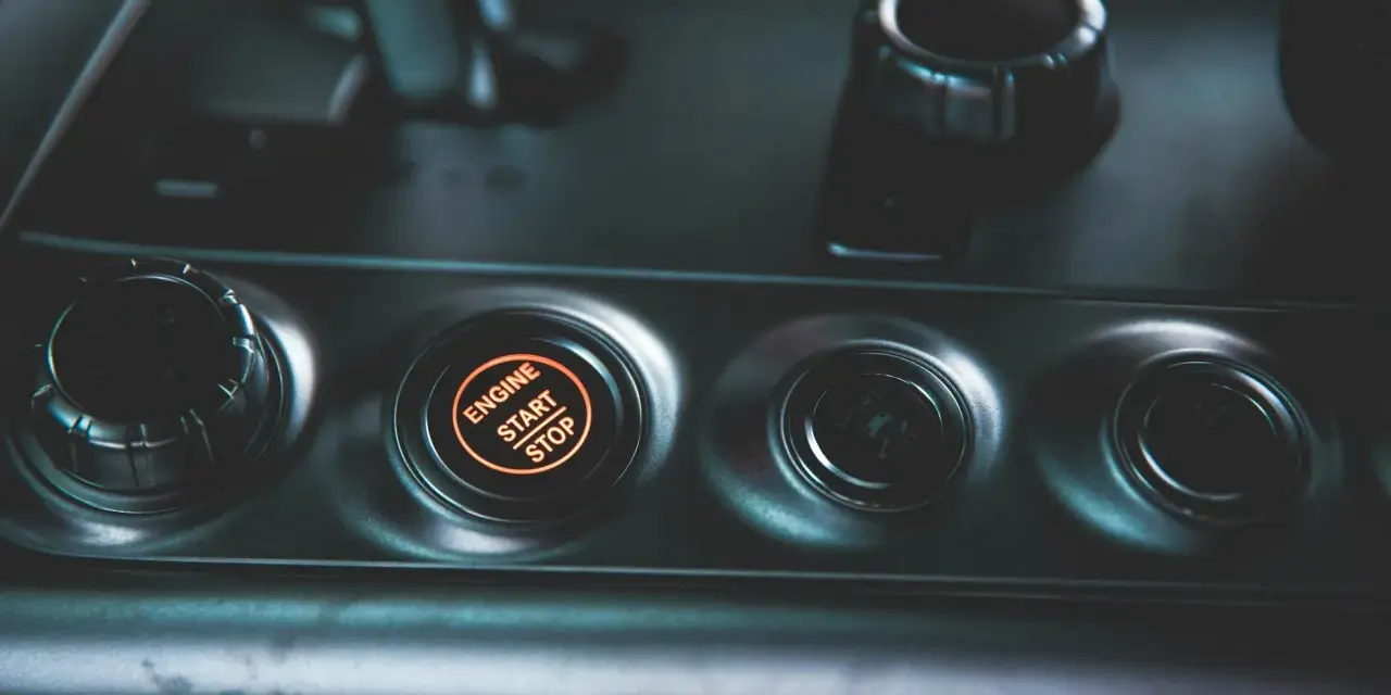 Podświetlany przycisk "ENGINE START STOP" w samochodzie. Obok niego pokrętło wyboru trybu jazdy, jak czujnik IBS.
