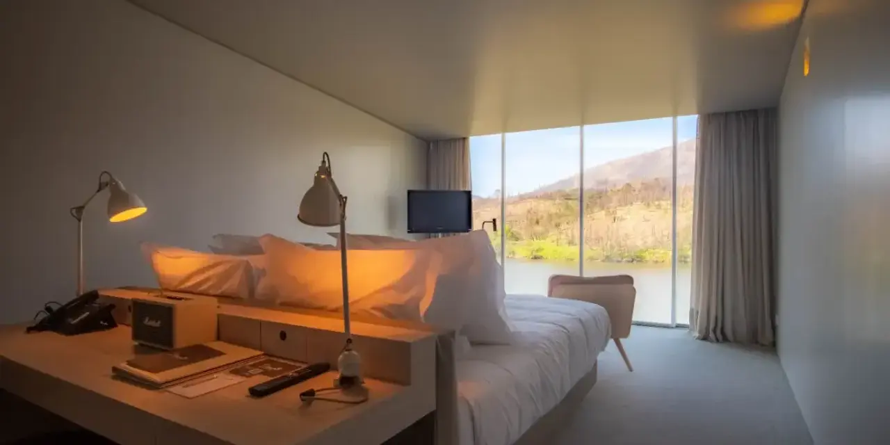 Un angolo studio in camera da letto con vista sul lago. Due lampade illuminano la scrivania con telefono e altoparlante.