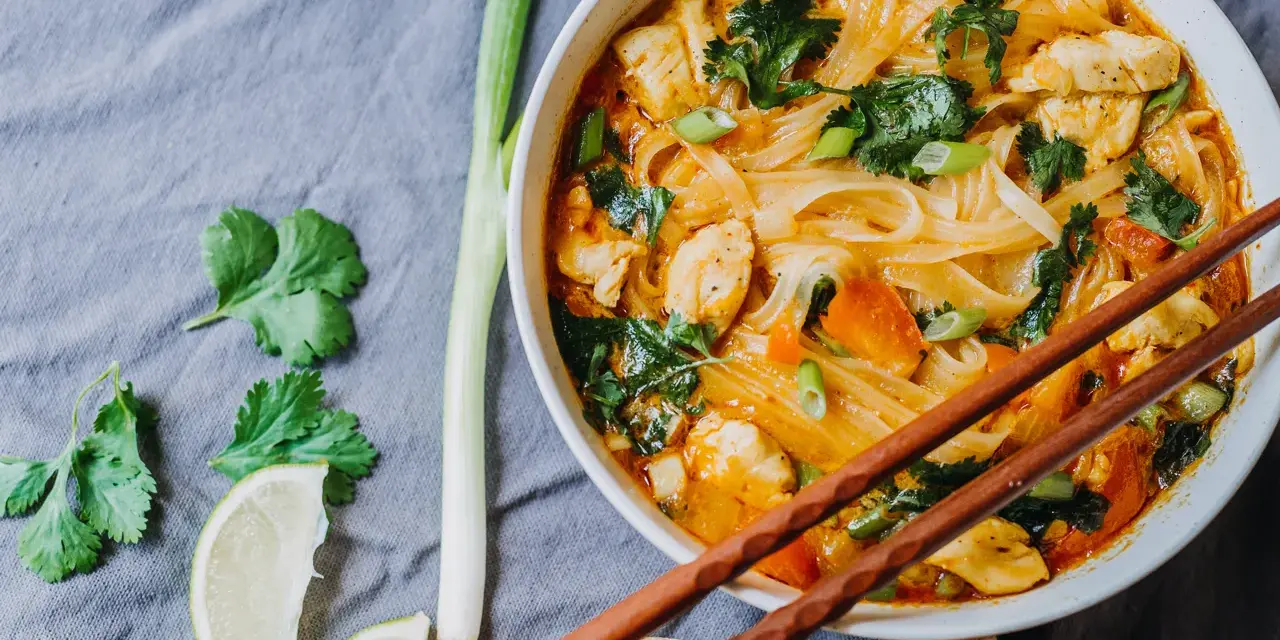 Miseczka z tajską zupą curry z kurczakiem, makaronem ryżowym i warzywami, podana z pałeczkami.