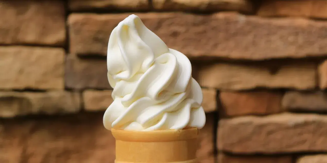 Ein cremiges Vanilleeis mit Ei im Waffelhörnchen, vor einer rustikalen Steinwand.
