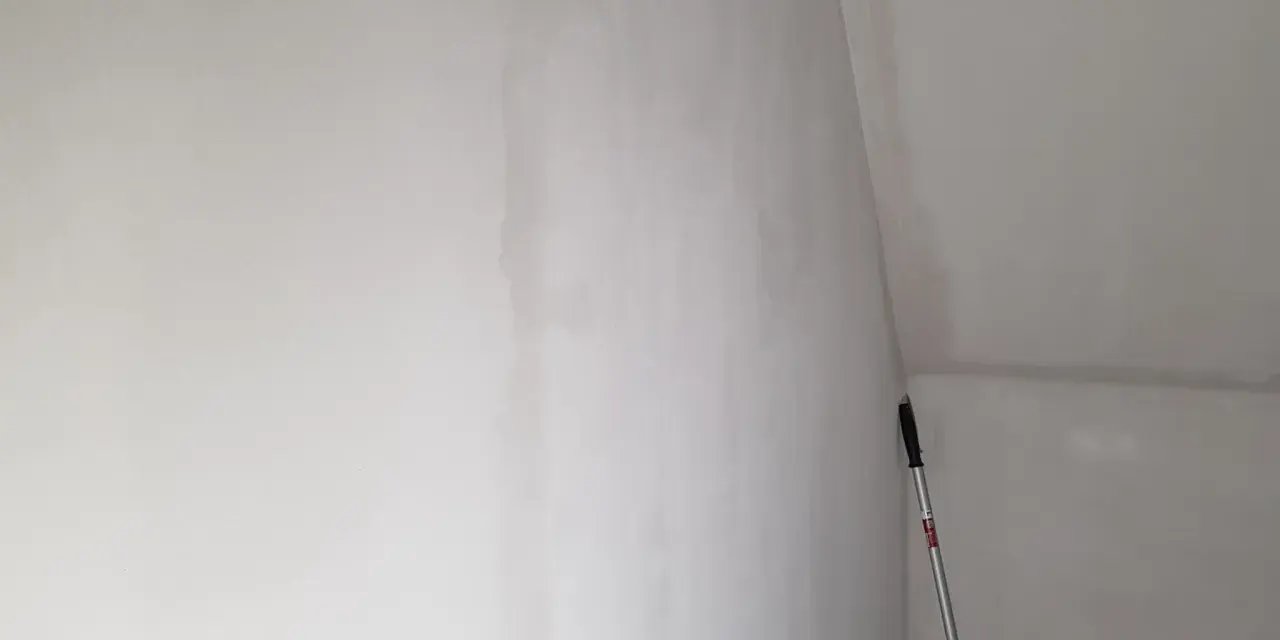 En lång skrapa med handtag står lutad mot en nyspacklad vägg, redo att slipa spackel för en slät yta.