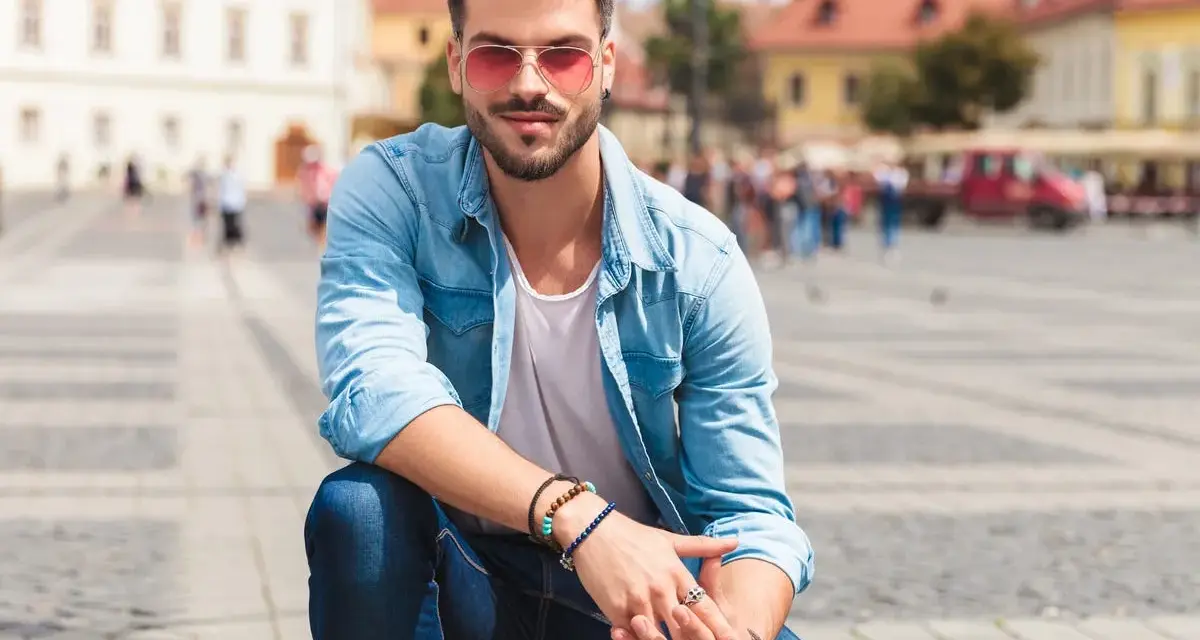 Uomo con occhiali da sole rosa e camicia di jeans, un'idea su come vestirsi in primavera uomo.