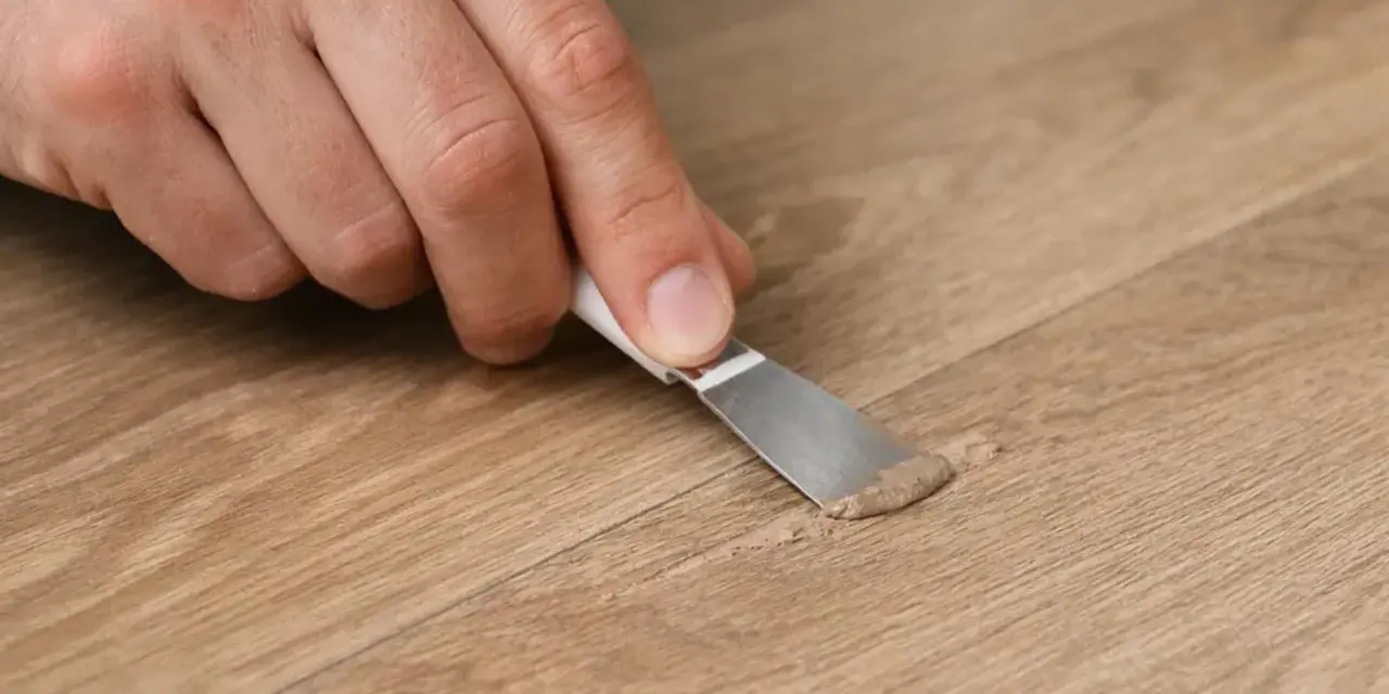 Mano che ripara un piccolo buco nel muro con una spatola e stucco.