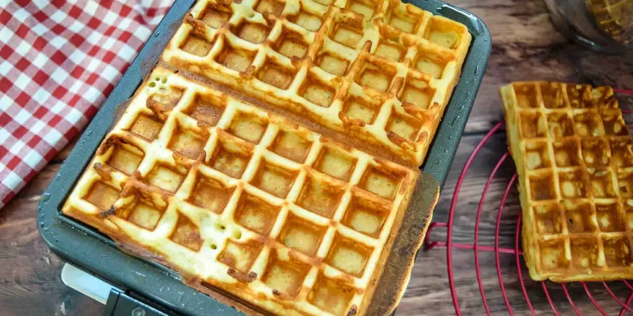 Frisch gebackene belgische Waffeln in einer Waffelform, daneben eine auf einem Rost.