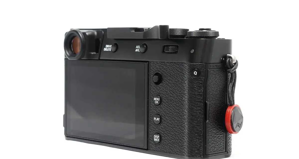 Czarne body aparatu Fujifilm X100S z widocznym ekranem, przyciskami i uchwytem na pasek.