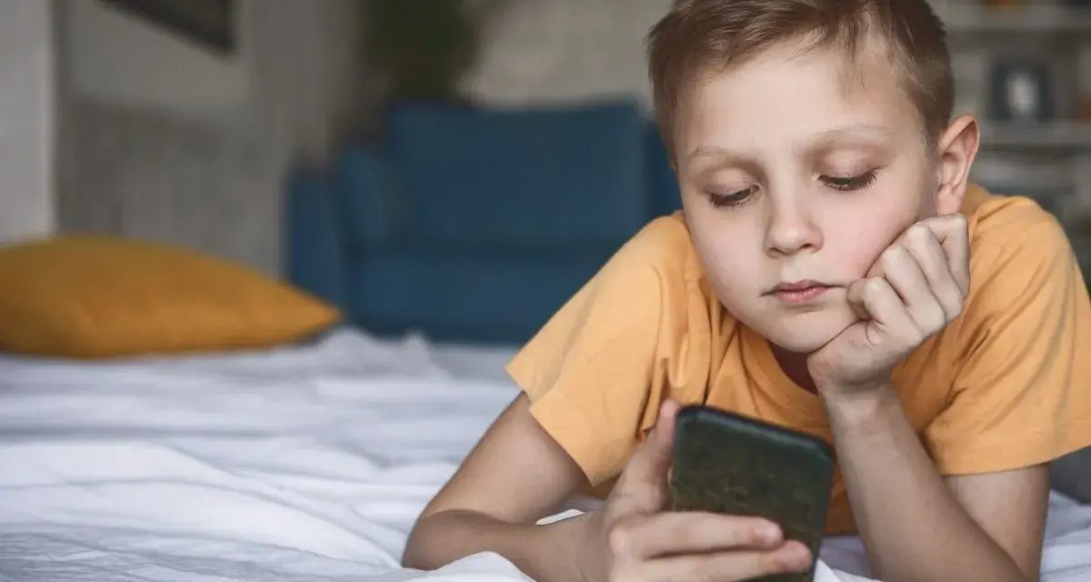 Chłopiec leży na łóżku, patrząc na telefon. Zastanawia się, co to jest sexting i jakie niesie zagrożenia.