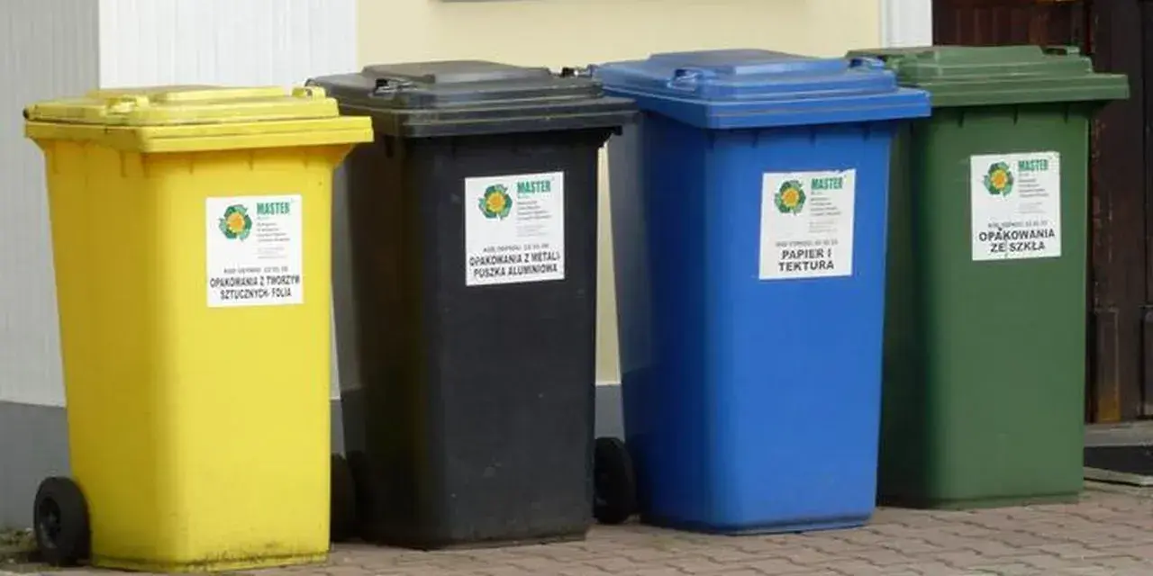 Cztery kolorowe kosze na śmieci: żółty, czarny, niebieski i zielony, stojące obok siebie.