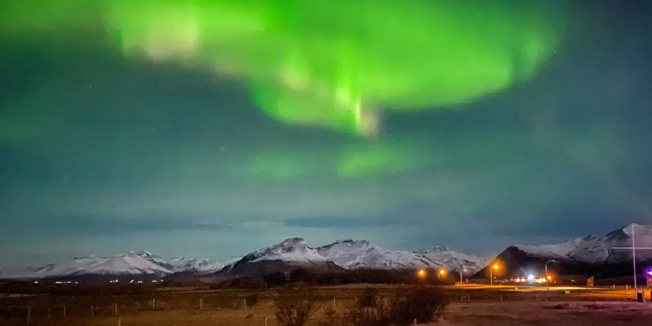 Islandia pogoda luty: zielona zorza polarna nad ośnieżonymi górami i polami.