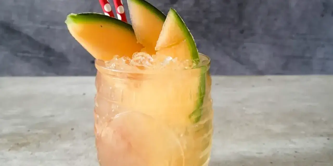 Orzeźwiający drink z mango, ozdobiony plasterkami owocu i dwoma czerwono-białymi słomkami. Idealny na upalne dni.