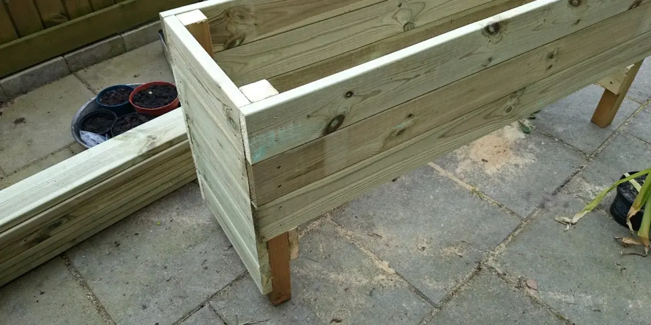 Påbörjat projekt att bygga blomlåda av tryckimpregnerat virke. Några krukor med jord står redo.