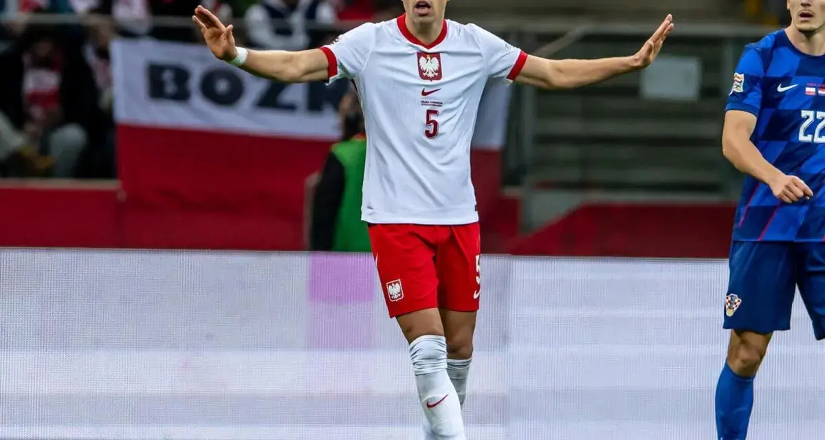 Piłkarz w białej koszulce z orłem, numer 5. Jan Bednarek po kontuzji wraca do gry, gestem prosi o spokój.