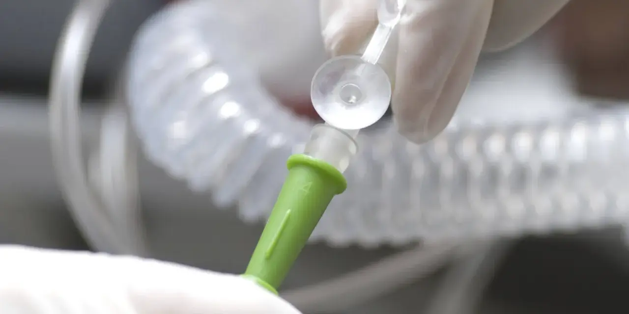 Hände in Handschuhen verbinden ein medizinisches Schlauchsystem. Mögliche Nachteile einer PEG-Sonde sind Infektionen und Verstopfungen.