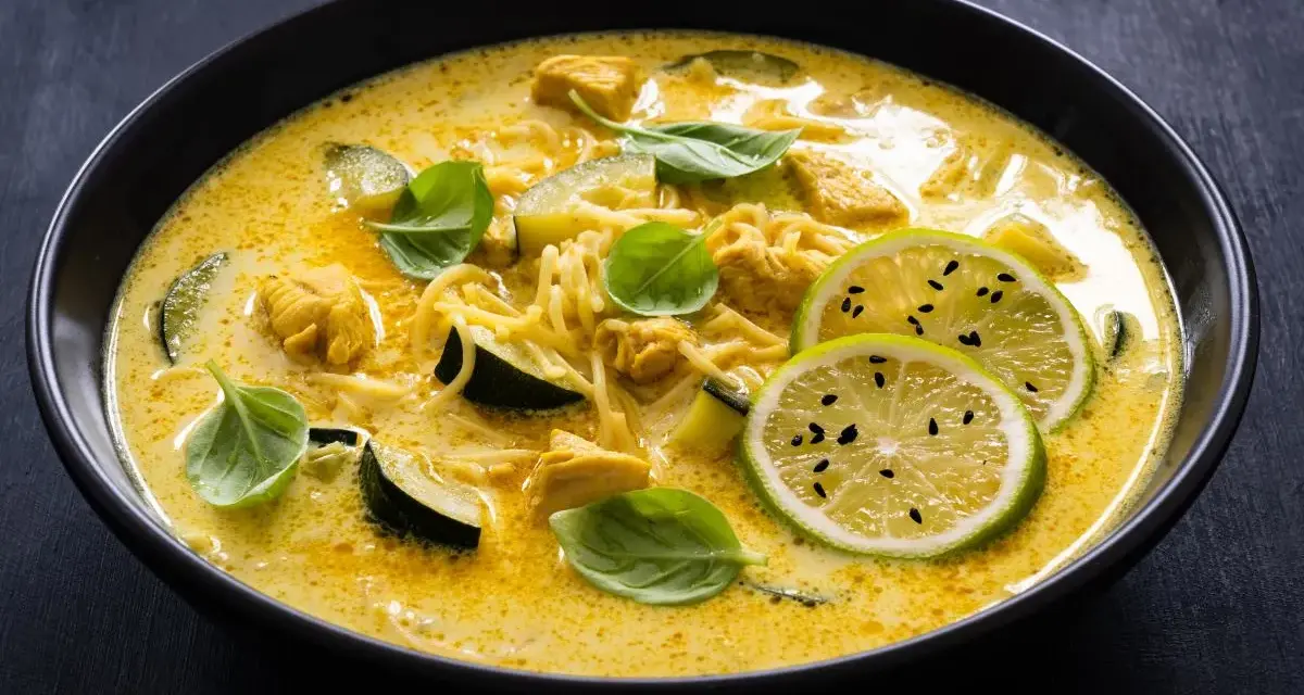 Aksamitne curry z kurczakiem, makaronem i plasterkami cukinii, ozdobione świeżą bazylią i limonką.