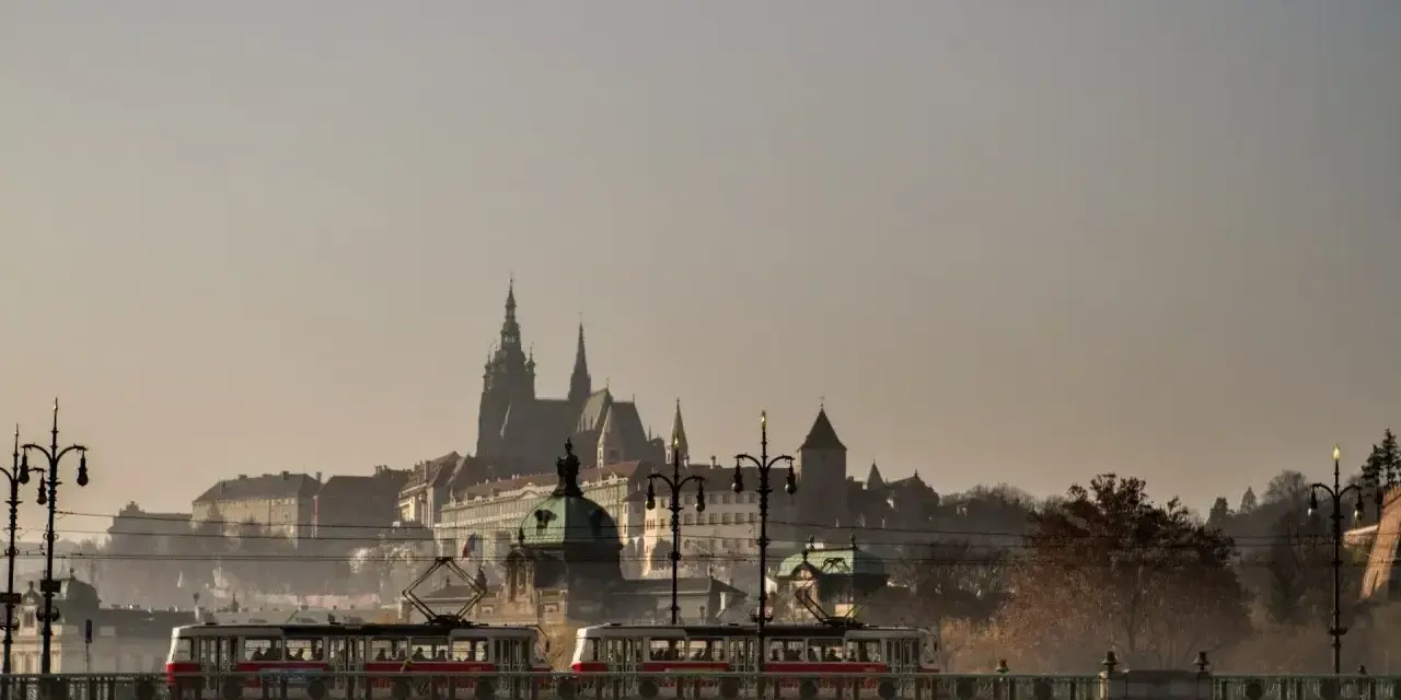 Most w Czechach, po którym przejeżdża tramwaj, z widokiem na zabytkowe budowle w oddali.