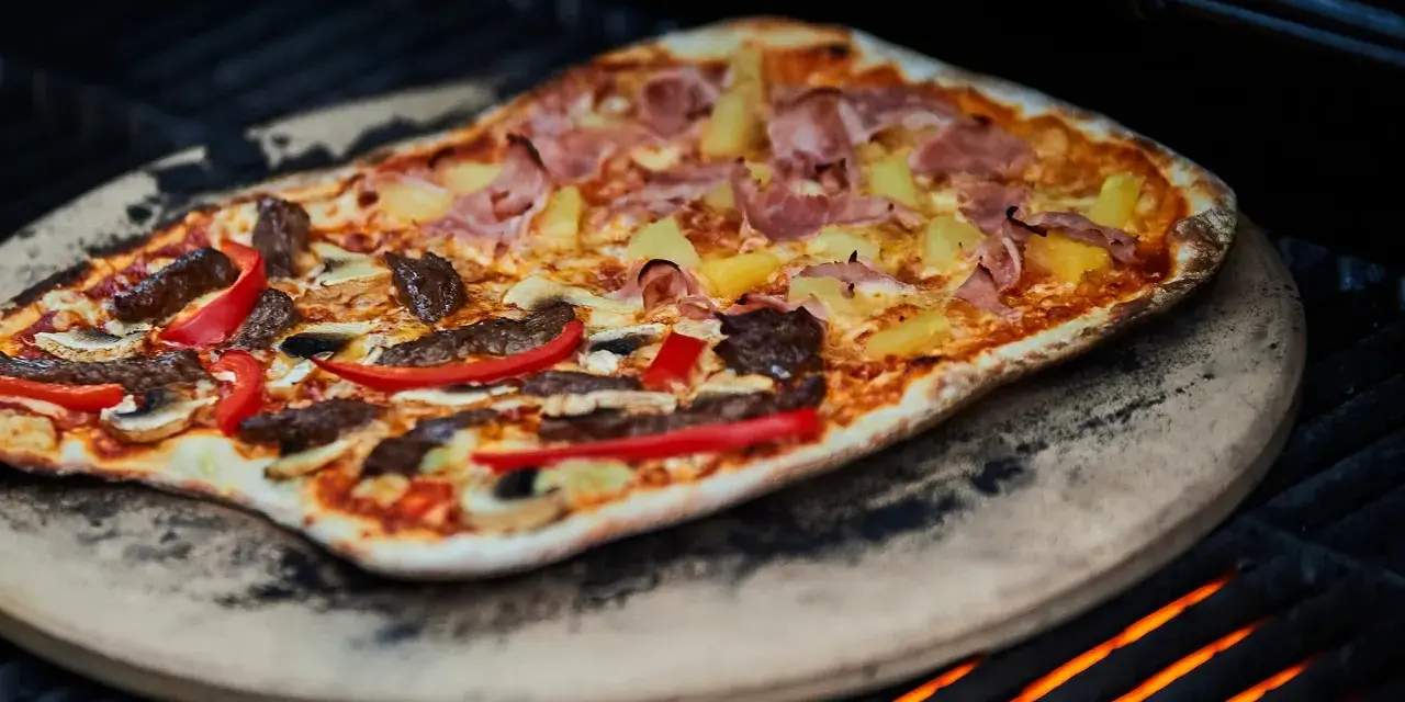 En läcker pizza på grillen med skinka, ananas, kött och paprika. En perfekt sommarmåltid!