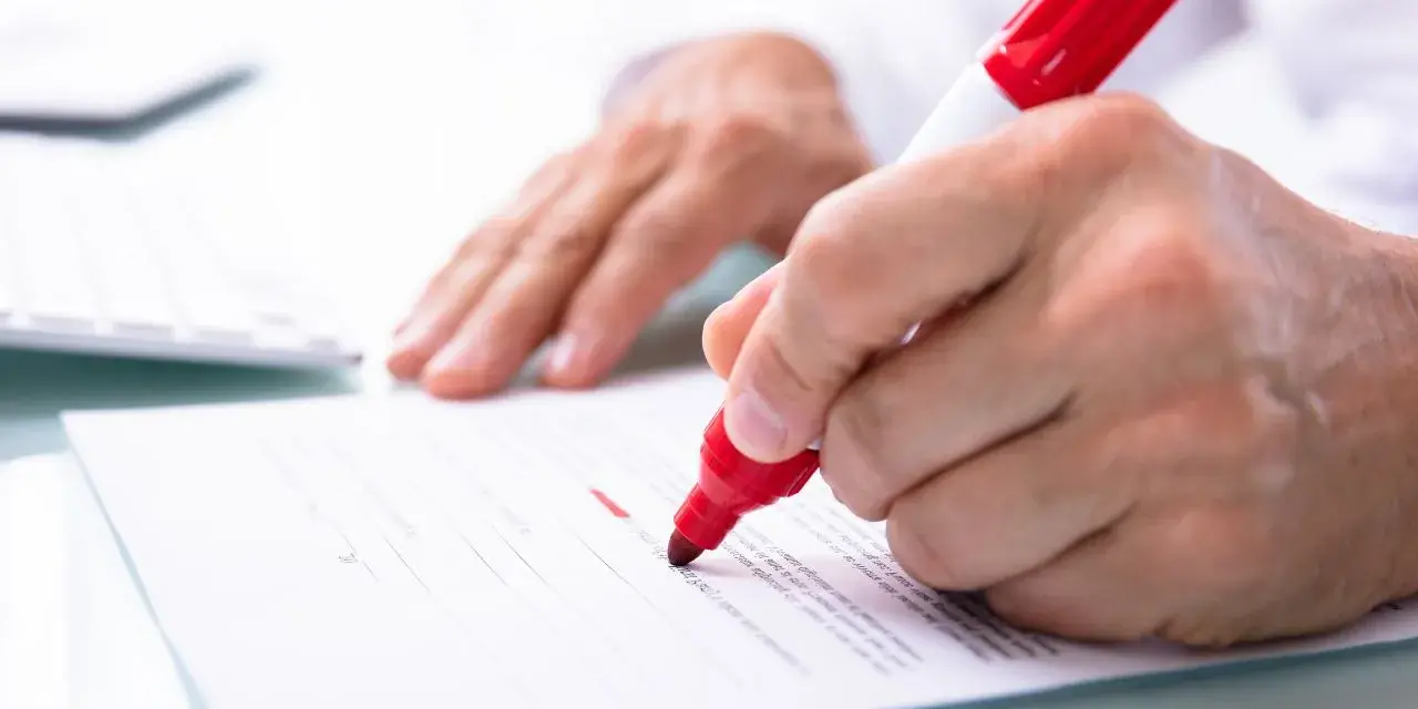 Ręka zaznacza czerwonym markerem potencjalne błędy w umowach kredytowych. VOTUM Consumer Care pomaga w analizie dokumentów.