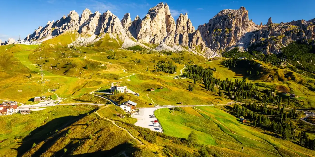 Panorami mozzafiato sull'**Alta Via numero 2 Dolomiti**. Sentieri serpeggianti tra prati verdi e imponenti vette rocciose sotto un cielo azzurro.