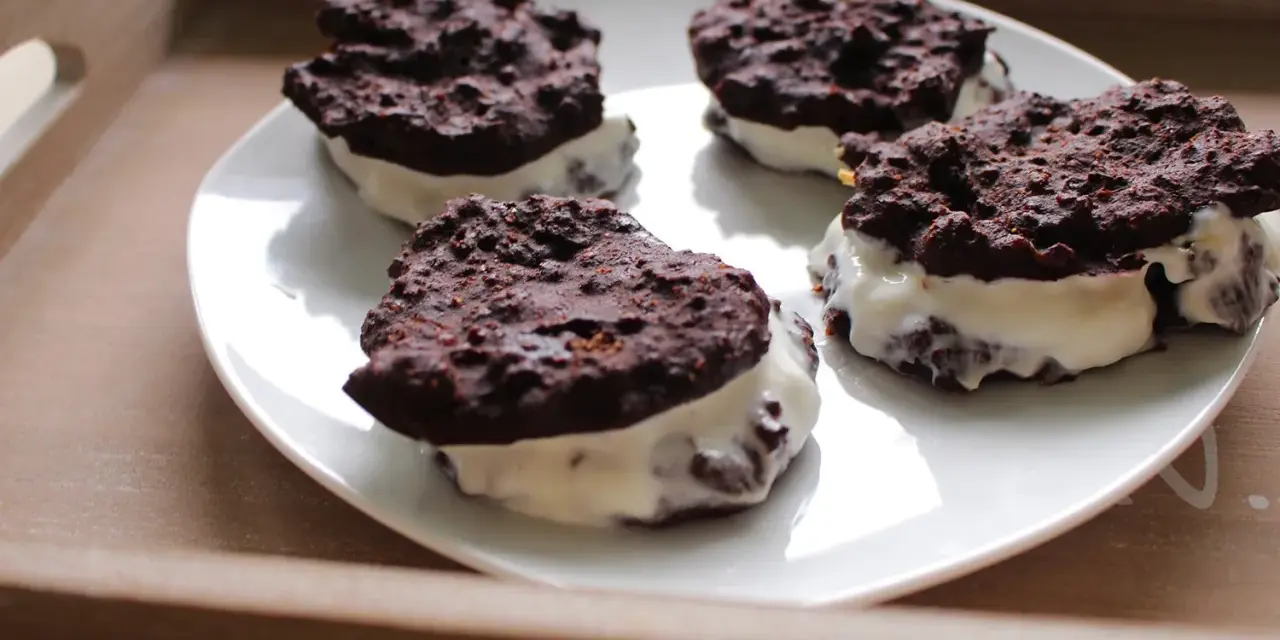 Cztery domowe ciastka z kremem, przypominające Oreo, na białym talerzu. Pyszna przekąska, choć warto sprawdzić oreo kcal przed zjedzeniem.