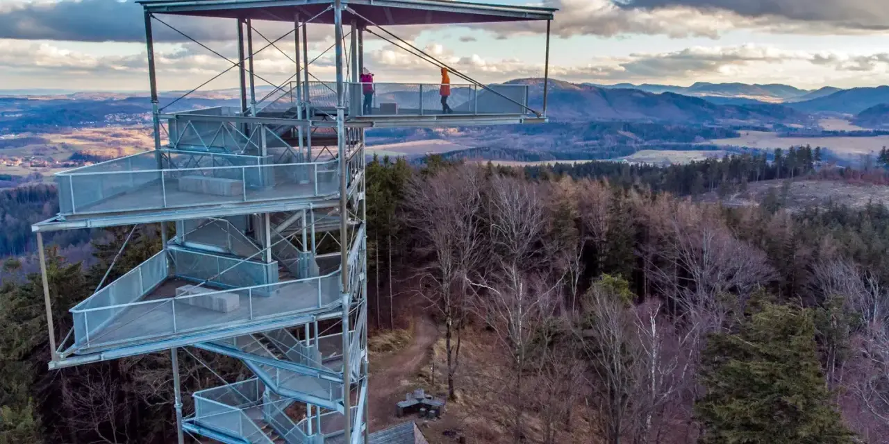 Trójgarb wieża widokowa. Jak dojechać? Metalowa konstrukcja z tarasami i schodami, otoczona lasem, z panoramą gór w tle.
