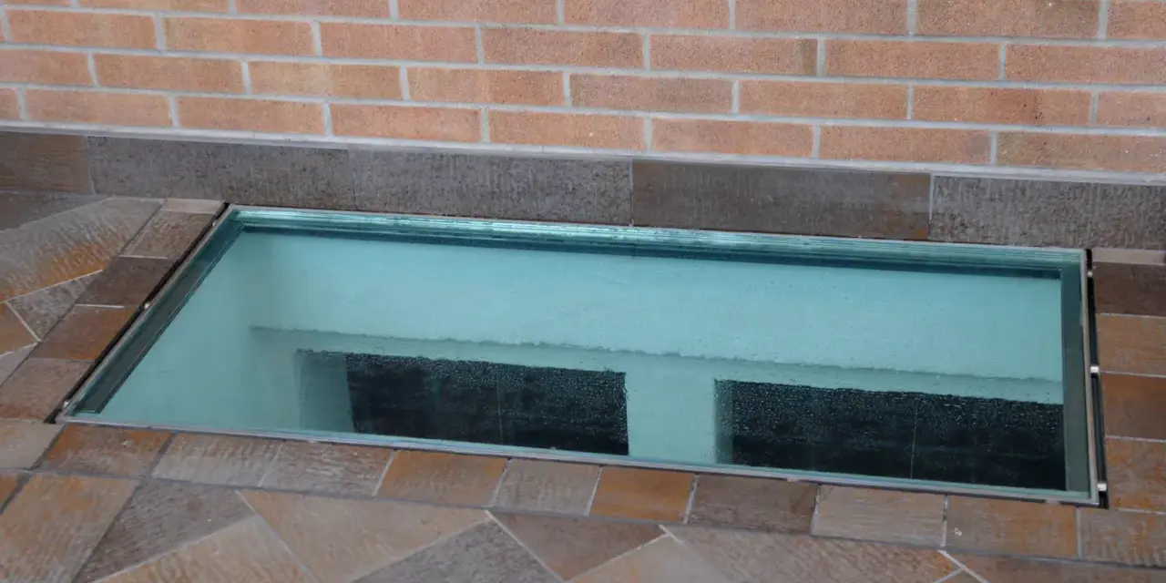 Bocche di lupo moderne in vetro, incastonate in un pavimento di piastrelle color terra, illuminano uno spazio sottostante.