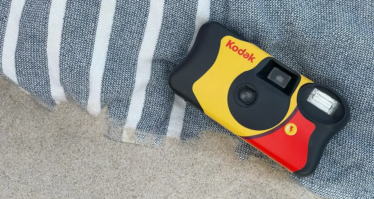 Aparat jednorazowy firmy Kodak leży na plaży obok ręcznika. Idealny do uchwycenia letnich wspomnień.