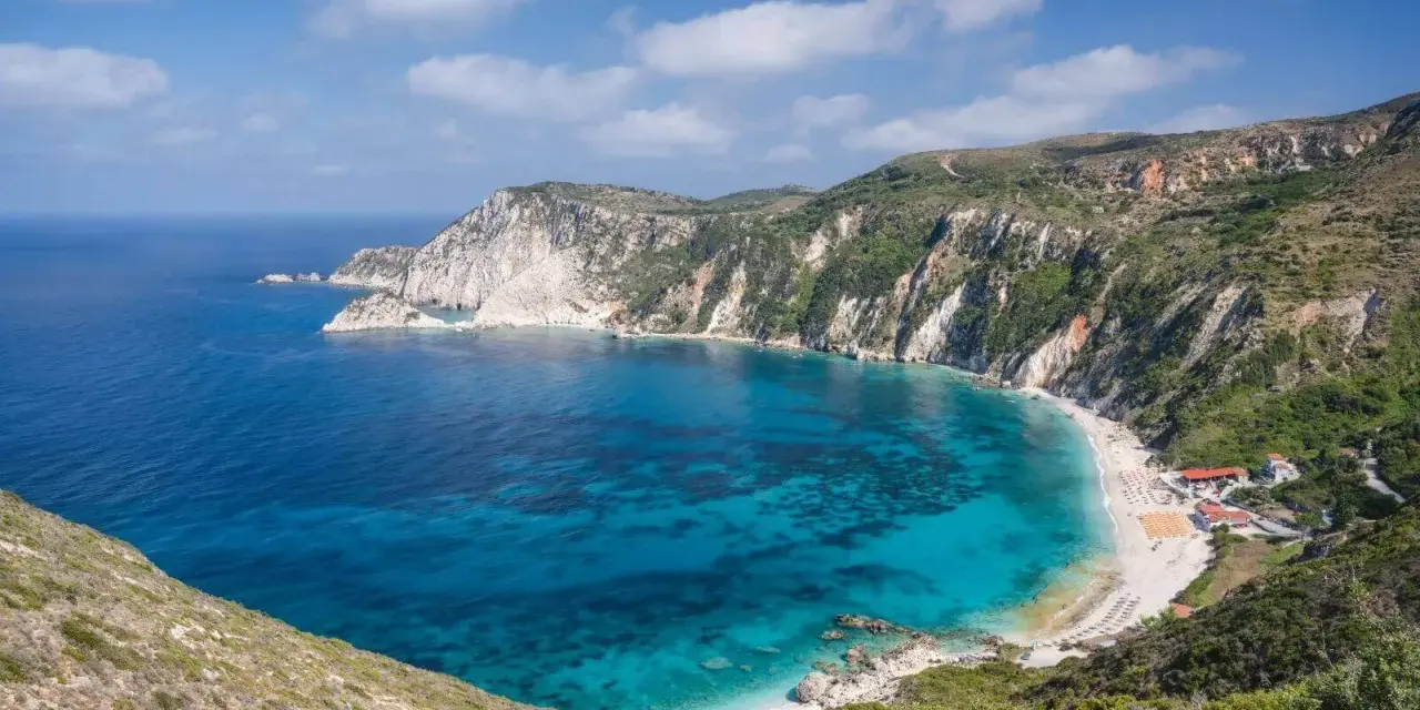 Malownicza zatoka z turkusową wodą i piaszczystą plażą, otoczona stromymi, zielonymi klifami. To idealne miejsce na wypoczynek na wyspie na Morzu Jońskim.