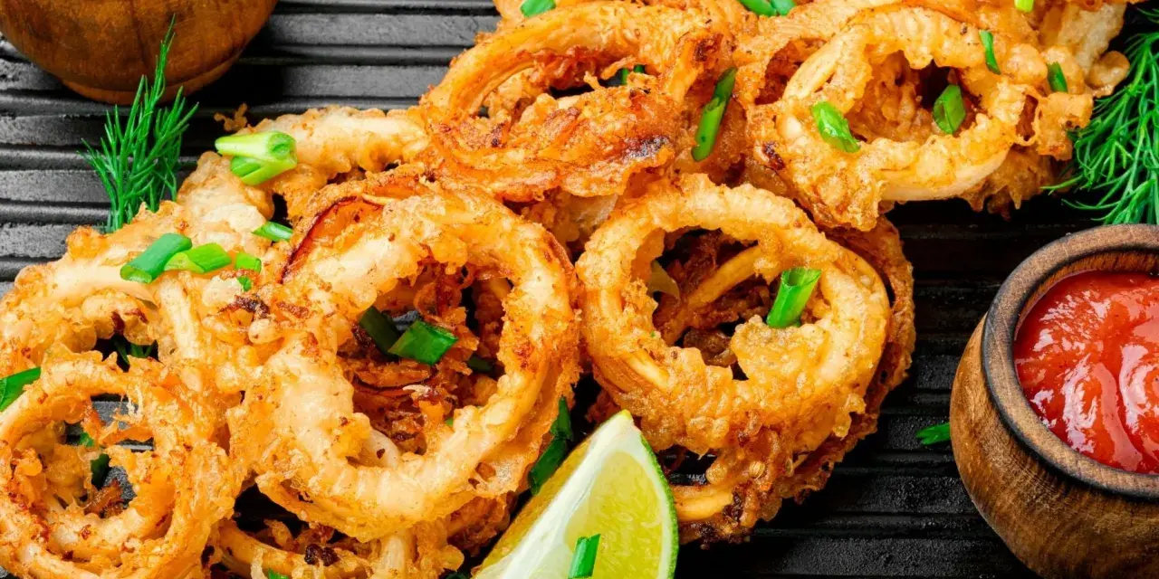 Aros de calamar rebozados y fritos, servidos con limón y salsa de tomate. Ideales para recetas con calamares.
