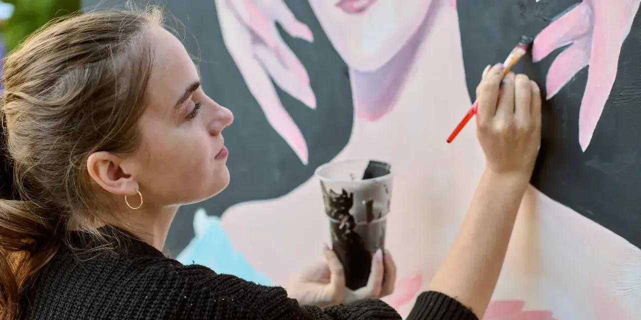 Une jeune artiste entrepreneur peint un portrait. Elle tient un pinceau et un gobelet de peinture noire.