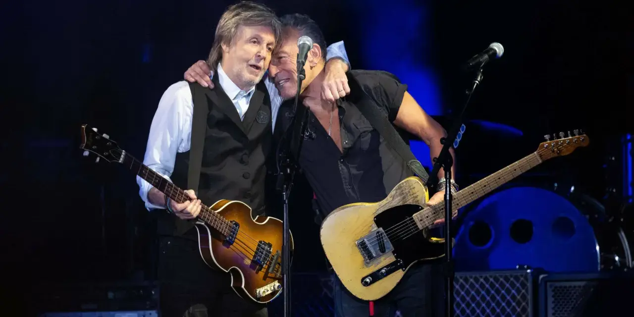 Bruce Springsteen und Paul McCartney umarmen sich auf der Bühne, beide mit Gitarren.