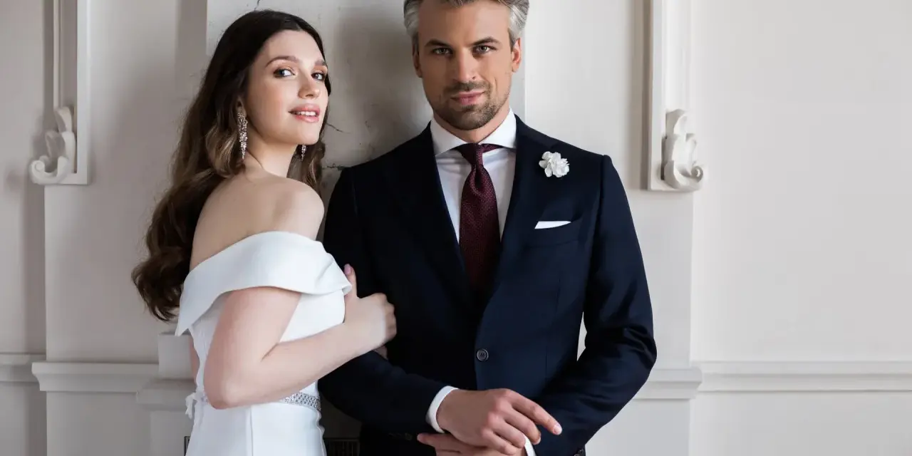 Elegancki pan młody ślub cywilny w granatowym garniturze i jego uśmiechnięta narzeczona w białej sukni.