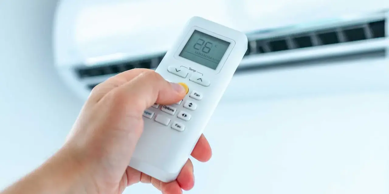 Dłoń trzymająca pilot do klimatyzatora, ustawiająca temperaturę. Ogrzewanie klimatyzatorem to komfort.