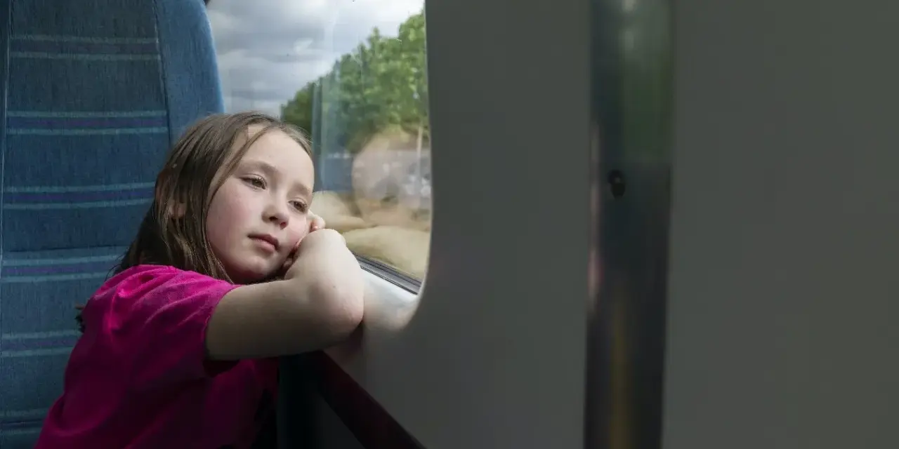 Dziewczynka wpatrzona w okno pociągu, zastanawia się, od ilu lat można jeździć samemu pociągiem.