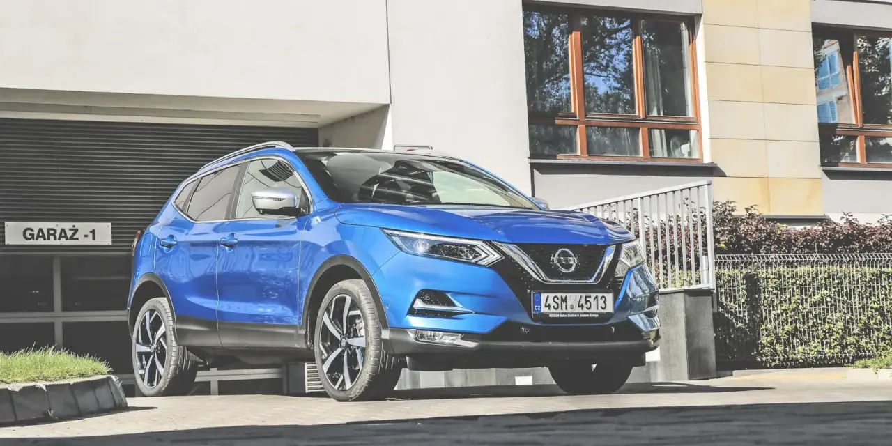 Błękitny Nissan Qashqai 2018 zaparkowany przed nowoczesnym budynkiem z garażem.