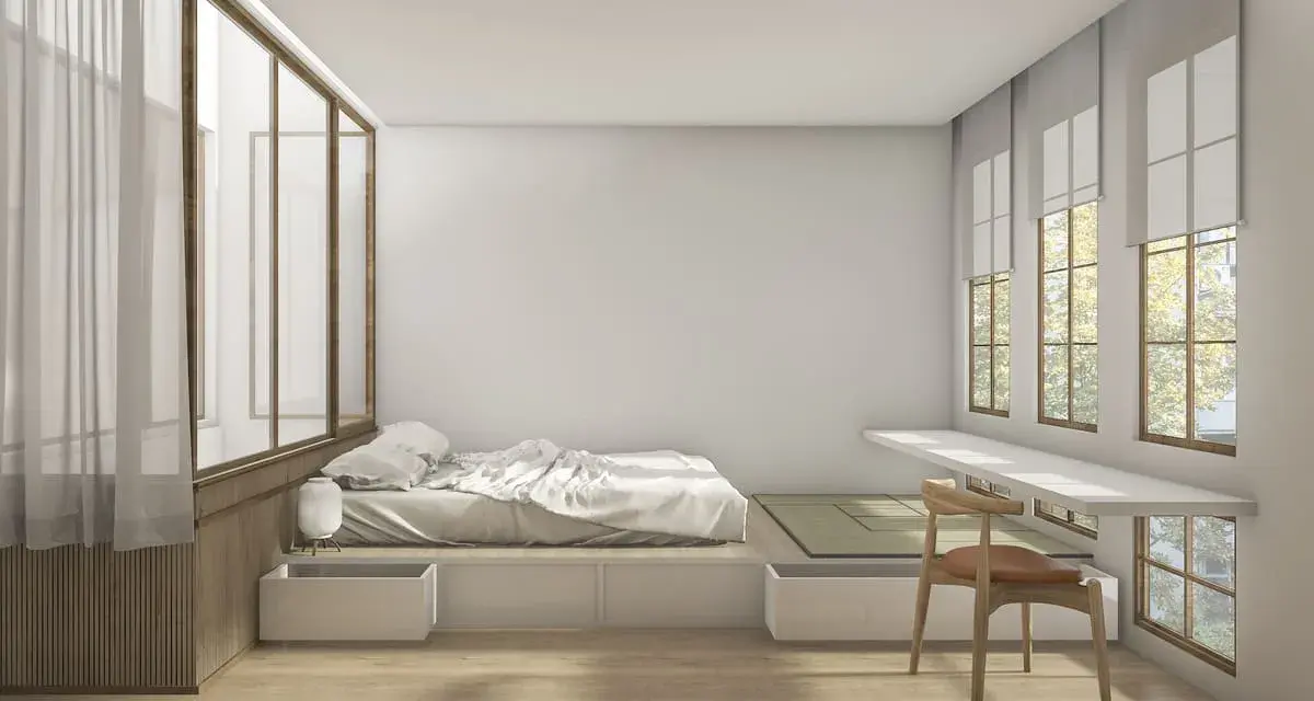 Camera da letto minimalista con letto feng shui, tatami, scrivania a muro e grandi finestre con vista su alberi.