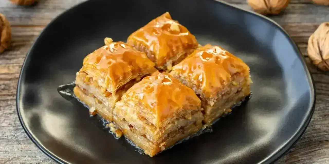 Słodka baklawa na czarnym talerzu, idealna do domowego przepisu. Orzechy włoskie w tle.
