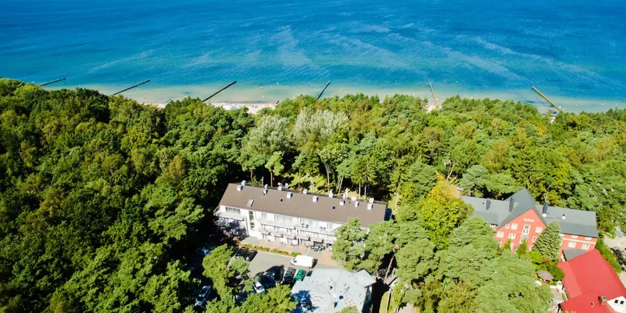 Widok z lotu ptaka na hotel otoczony lasem, z widokiem na morze. Idealne miejsce na wakacje, sprawdź nasz tui kod rabatowy!