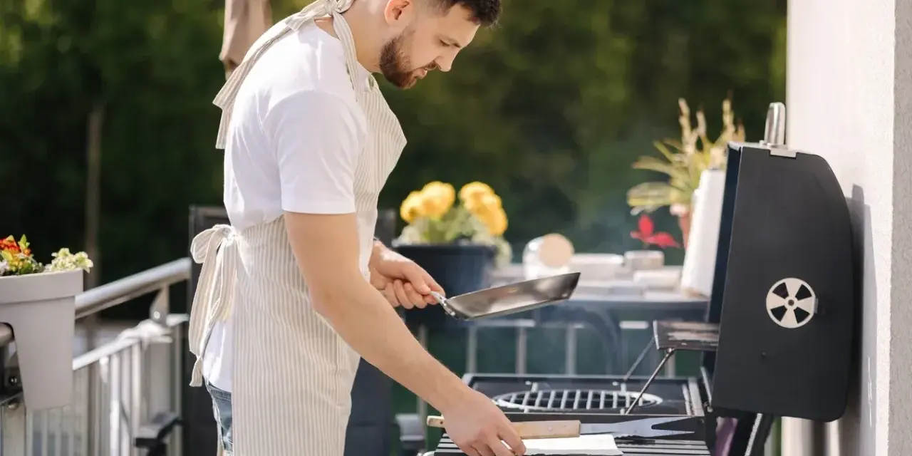 Mężczyzna w fartuchu przygotowuje grilla na balkonie, co pokazuje, że można robić grilla na balkonie.