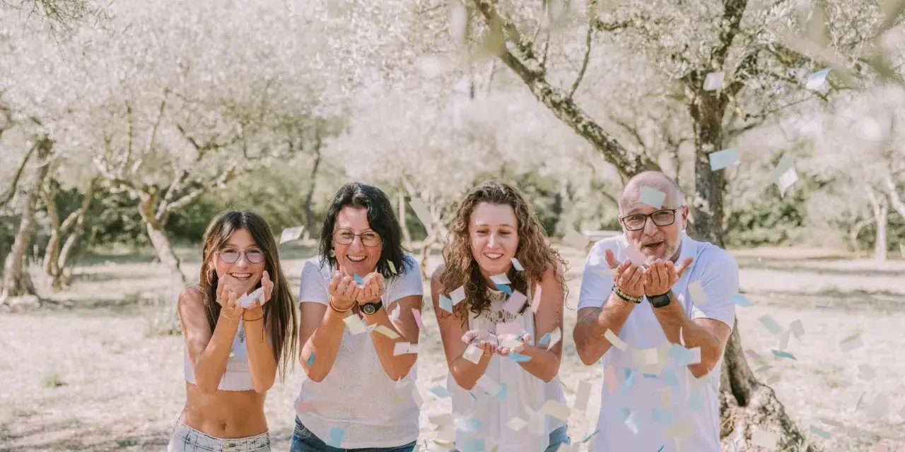 Photographie lifestyle : une famille lance des confettis sous des arbres fleuris, un moment de joie capturé.