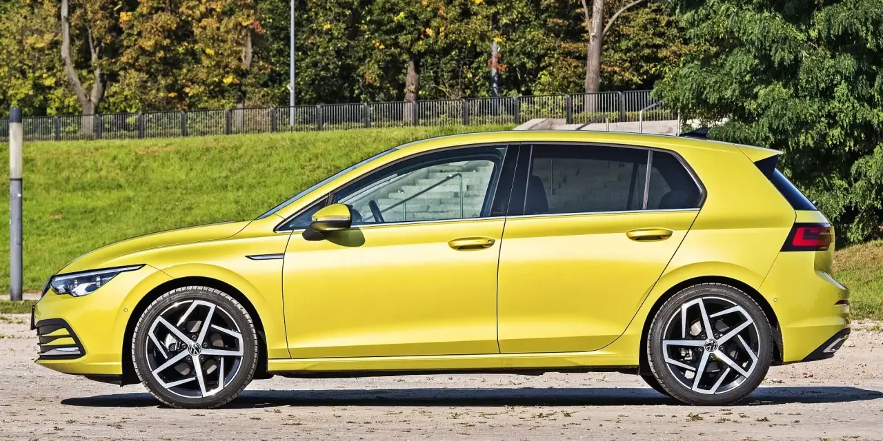 Żółty hatchback Volkswagen Golf VIII z przyciemnianymi szybami stoi na tle zieleni i drzew.