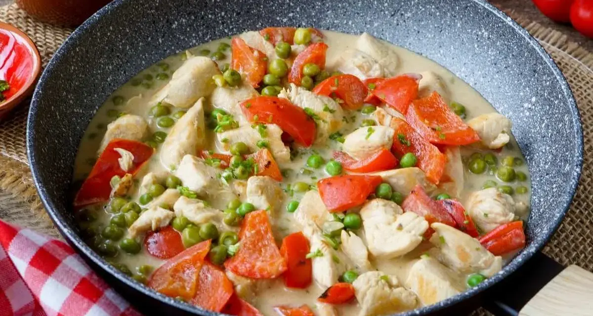 Hähnchen-Curry mit Erbsen und Paprika in cremiger Sauce – ein leckeres und gesundes Mittagessen, serviert in einer Pfanne.