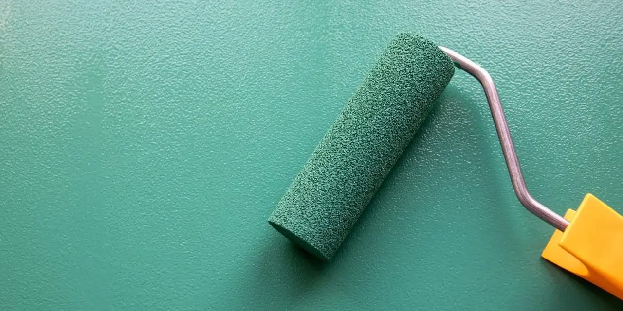 Rodillo de pintura verde sobre pared texturizada. Se puede pintar sobre papel pintado para renovar espacios.