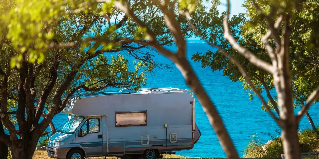 Kamper zaparkowany pod drzewami nad turkusowym morzem. Idealne miejsce na wakacje w Chorwacji kamperem.