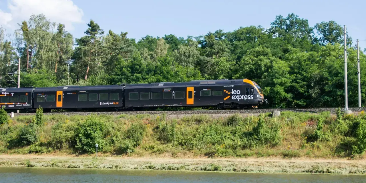 Czarny pociąg Leo Express z pomarańczowymi akcentami jedzie wzdłuż zielonego brzegu. Szukasz tanich biletów PKP Warszawa - Kraków?