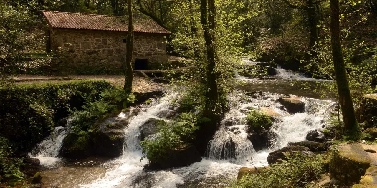 Antigua casa de piedra junto a un río con cascadas, ideal para una ruta senderismo Vigo.