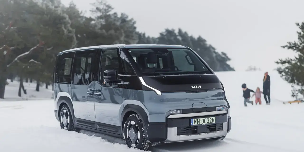 Szary elektryczny minivan Kia EV9 na śniegu, z rodziną w tle.